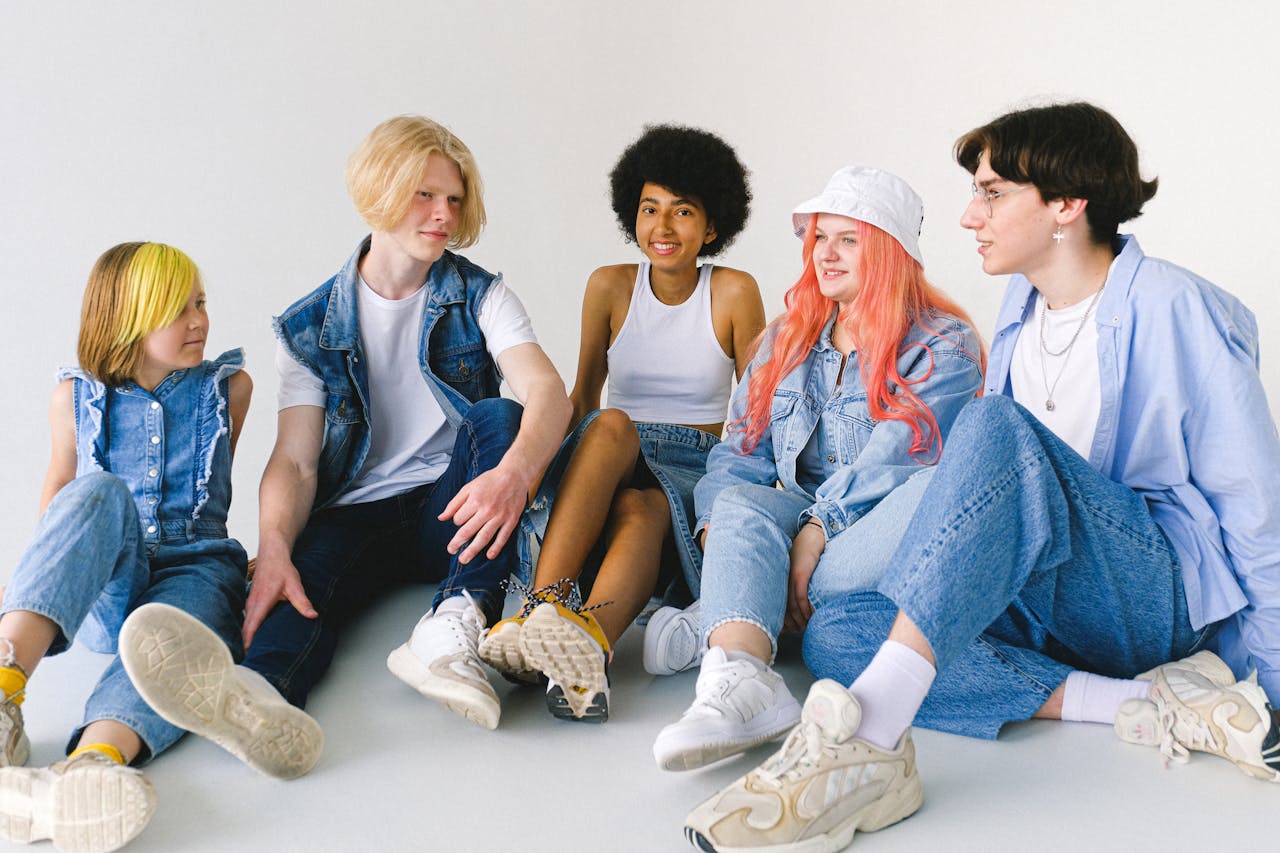Group of cheerful diverse teenager friends talking to each other while sitting together on floor against white background