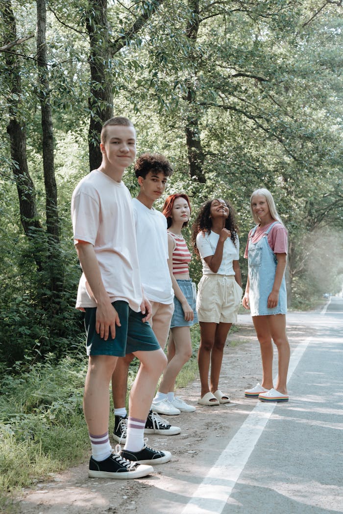 Diverse group of teens relaxing by a forest road, enjoying a sunny summer day.
